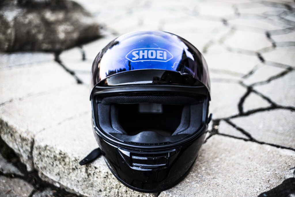 Image d'un casque de moto noir et mat avec une visière teintée légèrement relevée. Le casque est décoré de graphismes blancs et rouges, et est équipé d'une mentonnière et d'un système de ventilation. Le casque est posé sur une surface sombre et lisse, laissant apparaître ses contours nets et élégants